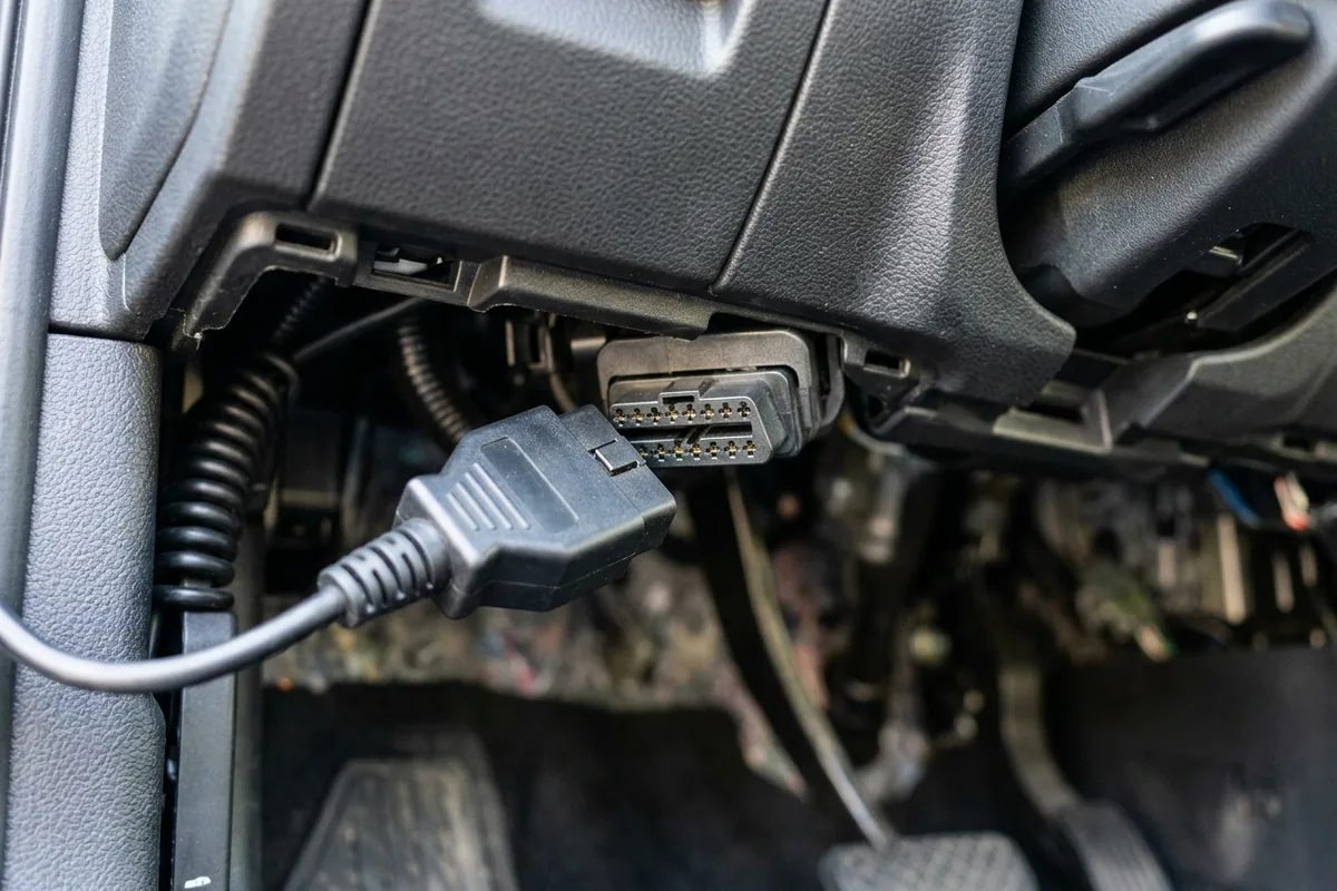 Handheld OBD-II scanner with a blank screen resting near the diagnostic port under a car dashboard
