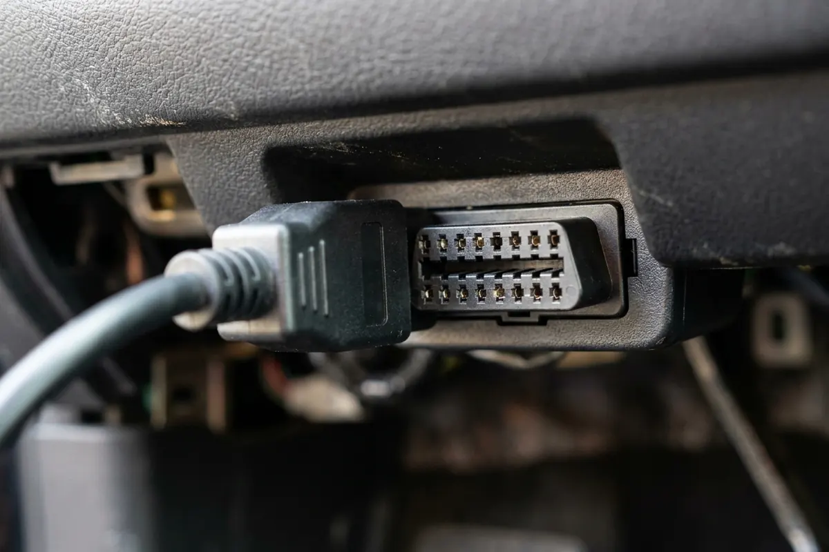 Handheld TPMS Relearn Tool by a Car Wheel Handheld TPMS relearn tool with a blank screen held next to a car wheel and tire in a garage
